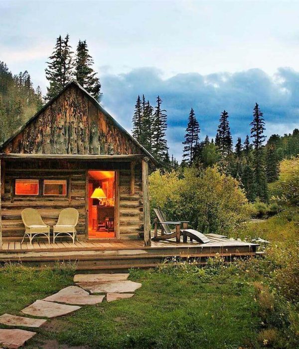 Cozy cabin glowing warmly in a lush mountain forest at dusk.